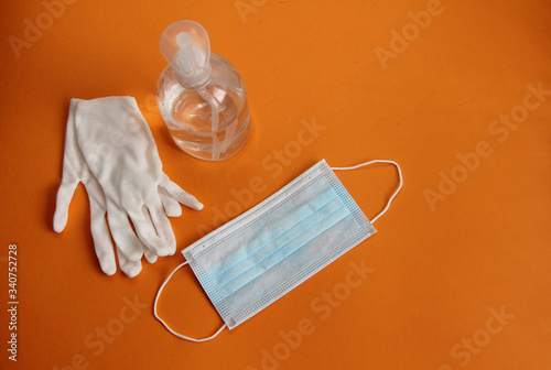 virus disinfection measures white protective gloves, sanitizer, protective mask isolated on an orange background