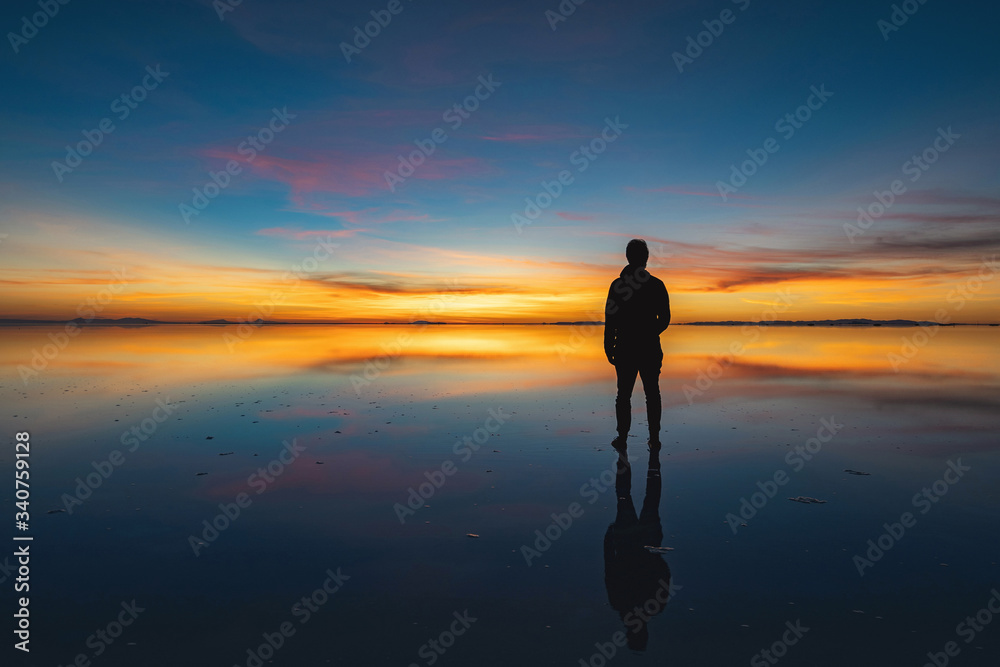 Moody shot of solo traveller looking at the horizon during sunrise at Uyuni Salt Flats (Spanish: Salar de Uyuni ) in Bolivia, South America.