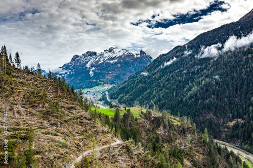 Aerial view of valley with green slopes of the mountains of Italy, Trentino, The trees tumbled down by a wind, huge clouds over a valley, green meadows, Dolomites on background, cloudy weather