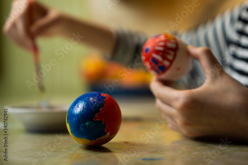 Hands of child girl in striped dress painting easter egg at kitchen table. Cosy home wooden kitchen easter traditions