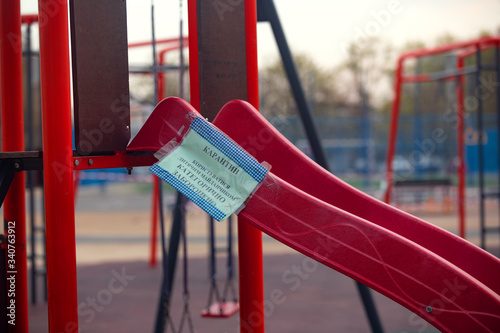 Kharkov, Ukraine, 18.04.2020:
Closed on 
quarantine by covid-19 kids playground with tied of white and red boundary tape in carantin time with warning 
sign, medium shot  photo