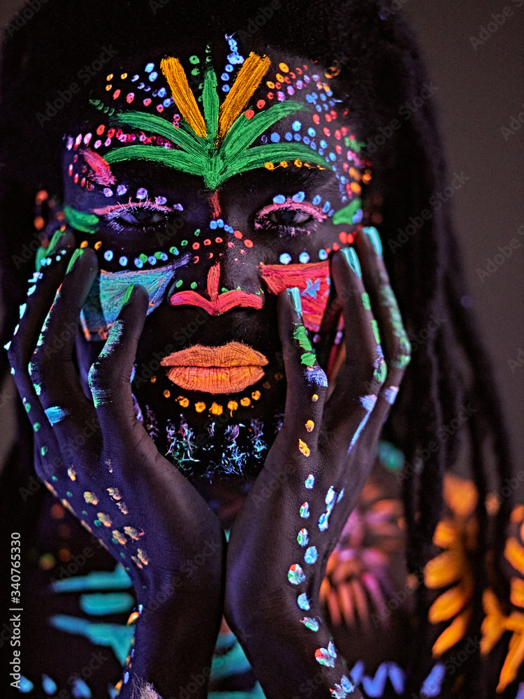 fantastic mysterious african male with UV body art posing at camera, futuristic body art, fluorescent paints glows in neon light