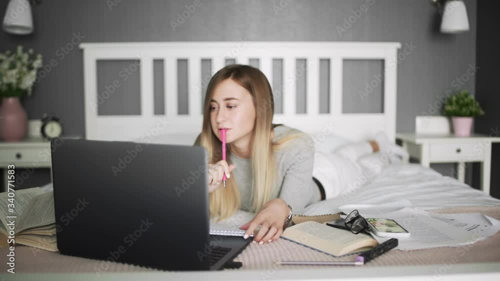 Young female student writes in notebook. On the bed distance learning for students. Coronavirus. Quarantine. Woman look at a laptop computer. Freelancer, distant work, work at home, online education Young female student writes in notebook. On the bed distance learning for students. Coronavirus. Quarantine. Woman look at a laptop computer. Freelancer, distant work, work at home, online education