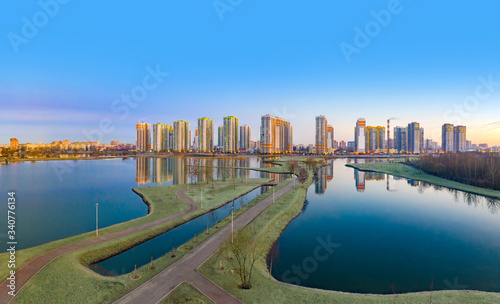 Residential complex on the shore of the lake. Modern urban architecture. Apartments in new buildings near the recreation area. Urban landscape. Ponds and houses under a blue sky.