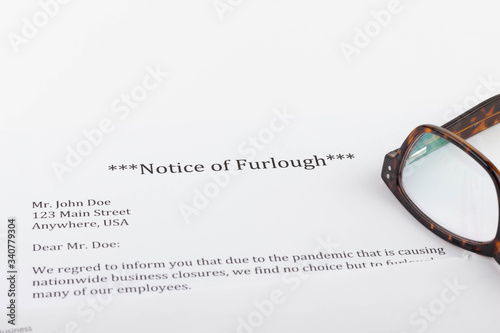 A notice of furlough lays on a table with an envelope, computer, notebook, and reading glasses.