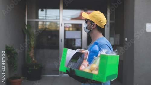 Wallpaper Mural Delivery guy with protective mask holding box / bag with groceries and POS for contactless payment. Torontodigital.ca