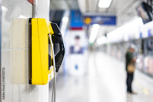 an emergency yellow land line phone cell on wall in public area of subway underground transport train station, concept of emergency calling situation on needing to contact people in urgent action