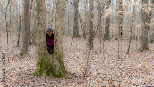 Asian woman in hat standing between a split tree trunk on a winter day
