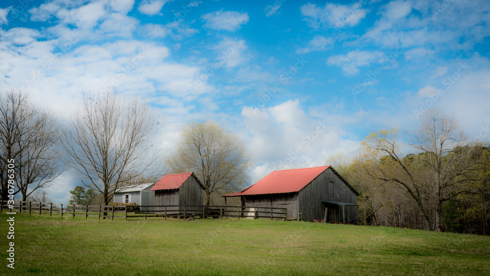 Small barns in a field with cloudy blue sky in the background Small barns in a field with cloudy blue sky in the background