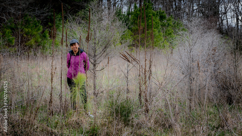 Woman in cap and purple coat standing amid the brush in a forest