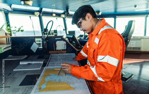 Filipino deck Officer on bridge of vessel or ship wearing coverall during navigaton watch at sea . He is plotting position on chart