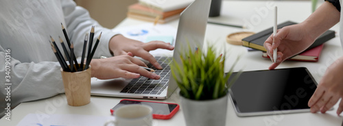 Cropped shot of two businesswoman working together with digital devices and office supplies on white table