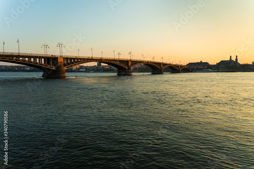 Die Theodor-Heuss-Brücke ragt umgeben vom wunderschön blauen Rhein im Sonnenuntergang in die mainzer Skyline © Simon Feller Media