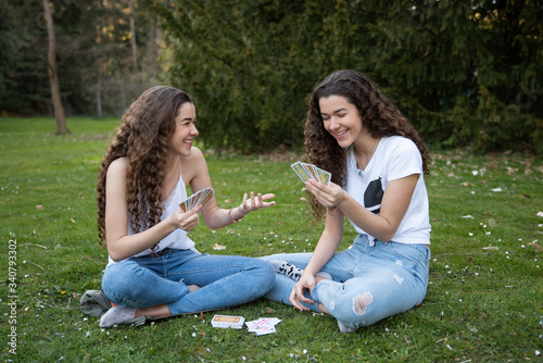 Twins sisters playing cards laying in the grass in a public park. © tomifj94