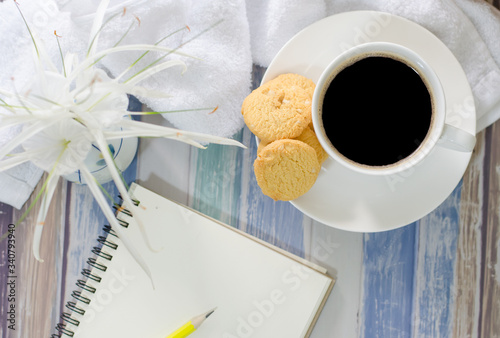 Top view a cup of hot coffee with .butter cookies,  notebook and flower on a wooden table holiday home vacation ideas