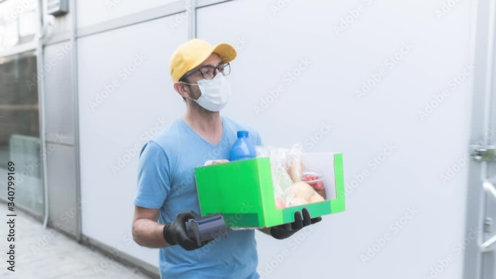 Delivery guy with protective mask holding box / bag with groceries and POS for contactless payment. Delivery guy with protective mask holding box / bag with groceries and POS for contactless payment.