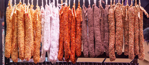 Fotografie Dried sausages sprinkled with various spices are hung in a row on a rack
