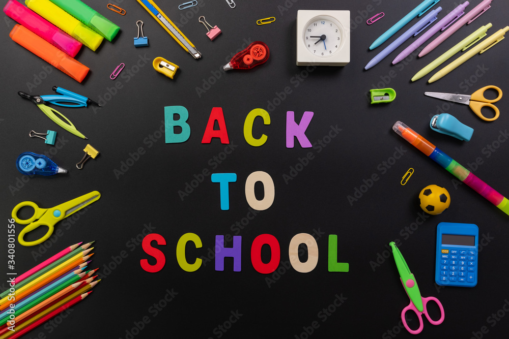 Back to school or Education concept. Top view of colorful school supplies with books, color pencils, calculator, pen, cutter, scissor, clips and alarm clock on chalkboard background.