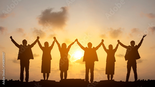 Silhouette of happy business teamwork making high hands over head in sunset sky background for business teamwork concept