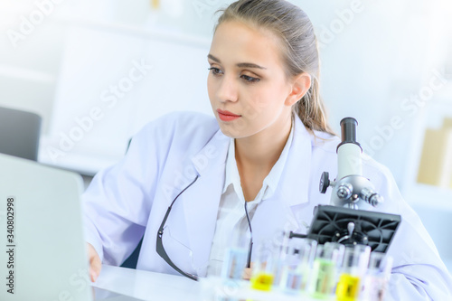 Young female scientist run an experiment or research in laboratory, with microscope and laptop. Medical healthcare technology, pharmaceutical research and development concept.