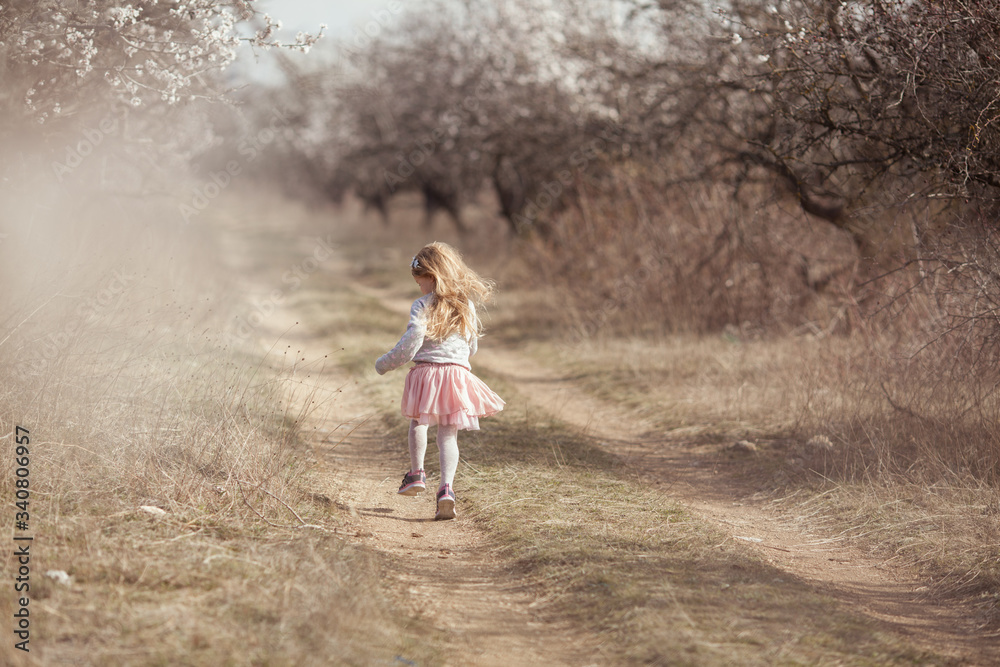 Happy beautiful girl runs in a flowering almond garden