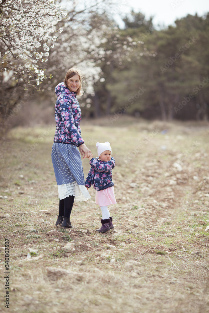 Portrait of happy mother and daughter on a background of almond trees in blossom, a woman and a child walk in the spring garden Portrait of happy mother and daughter on a background of almond trees in blossom, a woman and a child walk in the spring garden