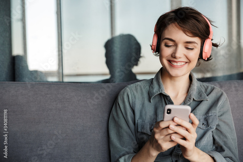 Image of nice young smiling woman using smartphone and headphones photo