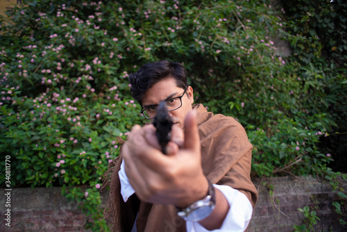 Blurred portrait of an young Indian Bengali detective with traditional wear pointing a gun in a winter morning in a crime scene.