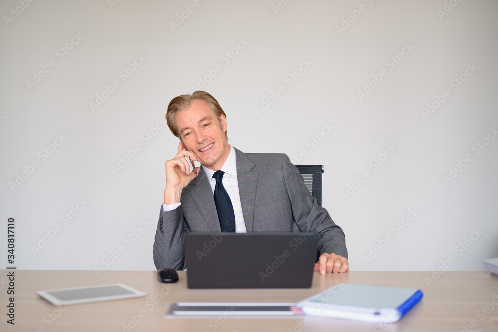 Happy mature businessman in suit talking on the phone at work Happy mature businessman in suit talking on the phone at work