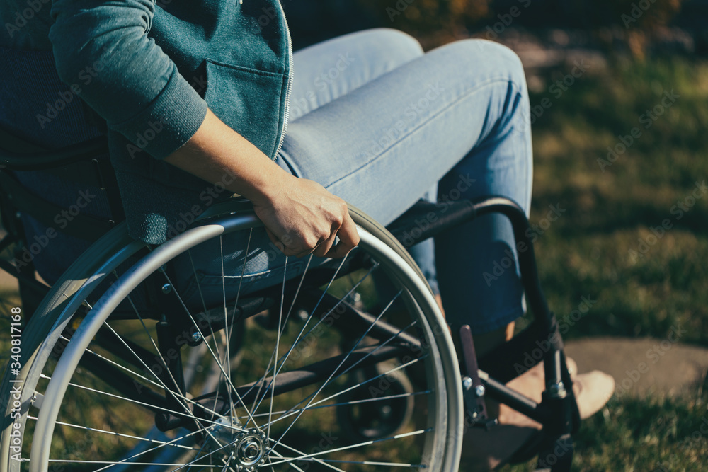 Obraz premium Close up of a young woman in a wheelchair while walking in a park on a sunny day. Recovery and healthcare concepts.