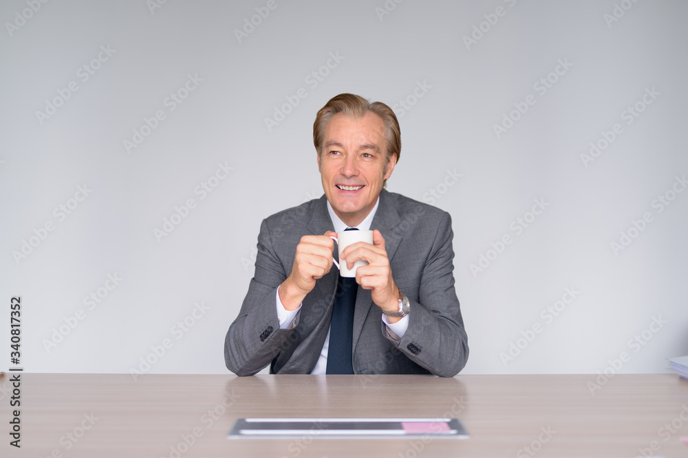 Happy mature handsome businessman thinking while drinking coffee at work Happy mature handsome businessman thinking while drinking coffee at work