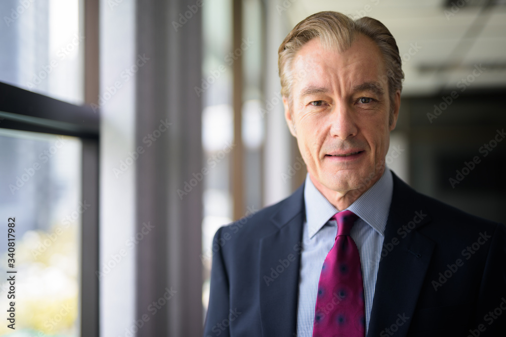 Face of happy mature handsome businessman in suit smiling by the window Face of happy mature handsome businessman in suit smiling by the window