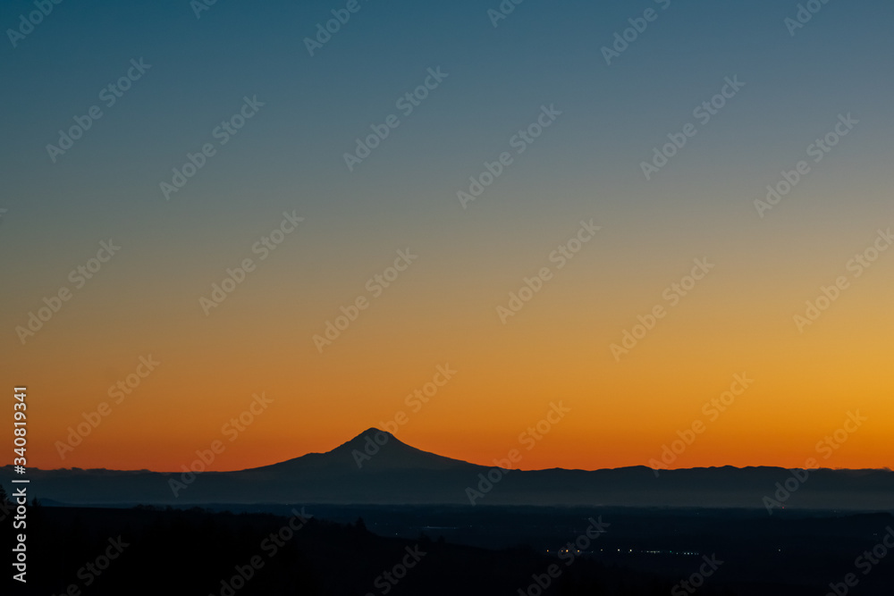 A sunrise scene in Oregon, with the iconic peak of Mt. Hood on the horizon in silhouette, vivid color behind. A sunrise scene in Oregon, with the iconic peak of Mt. Hood on the horizon in silhouette, vivid color behind.