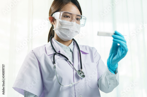 Doctor with blue gloves, surgical mask and glass looking on termometer