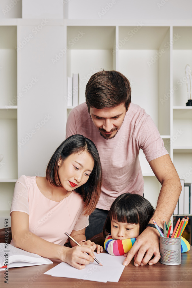 Father looking at his wife and daughter drawing pictures for kindergarten Father looking at his wife and daughter drawing pictures for kindergarten