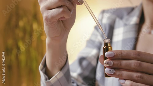 A beautiful young woman creates perfume in a glass bottle by combining several essential oils, close-up