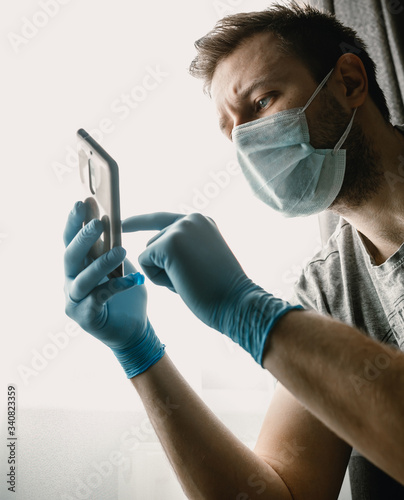 Man on self-isolation, quarantine at home. Looks at the phone.