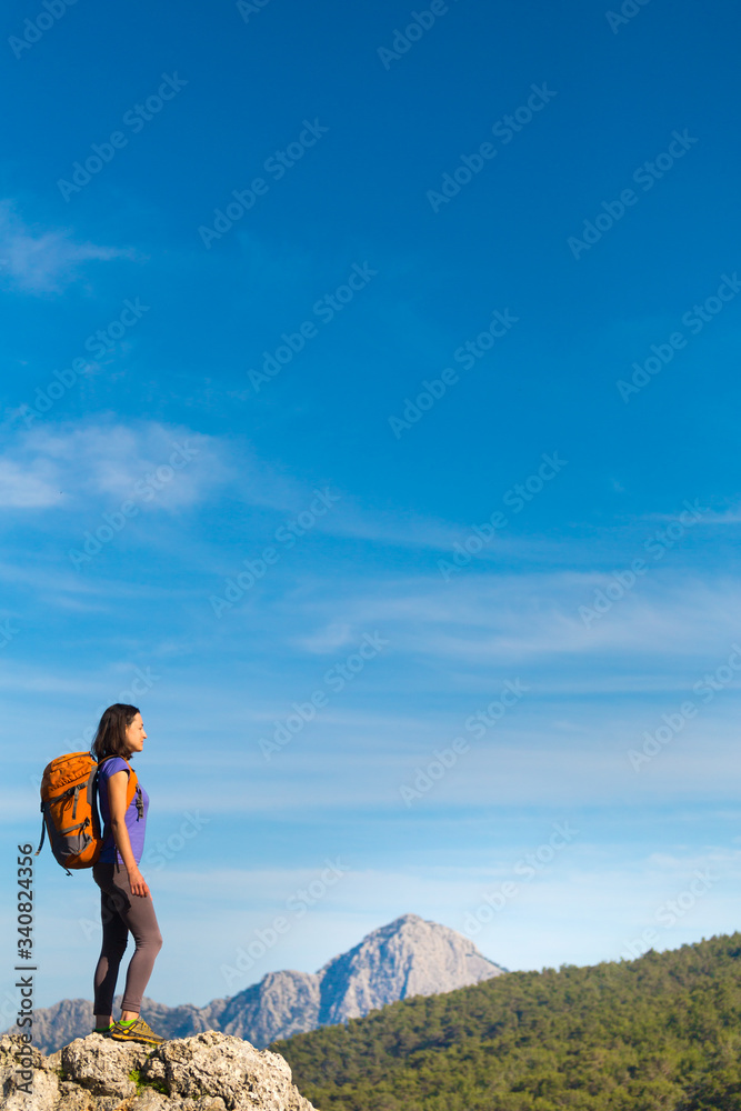 Naklejka premium A woman with a backpack stands on top of a mountain and admires the beauty of a mountain valley.