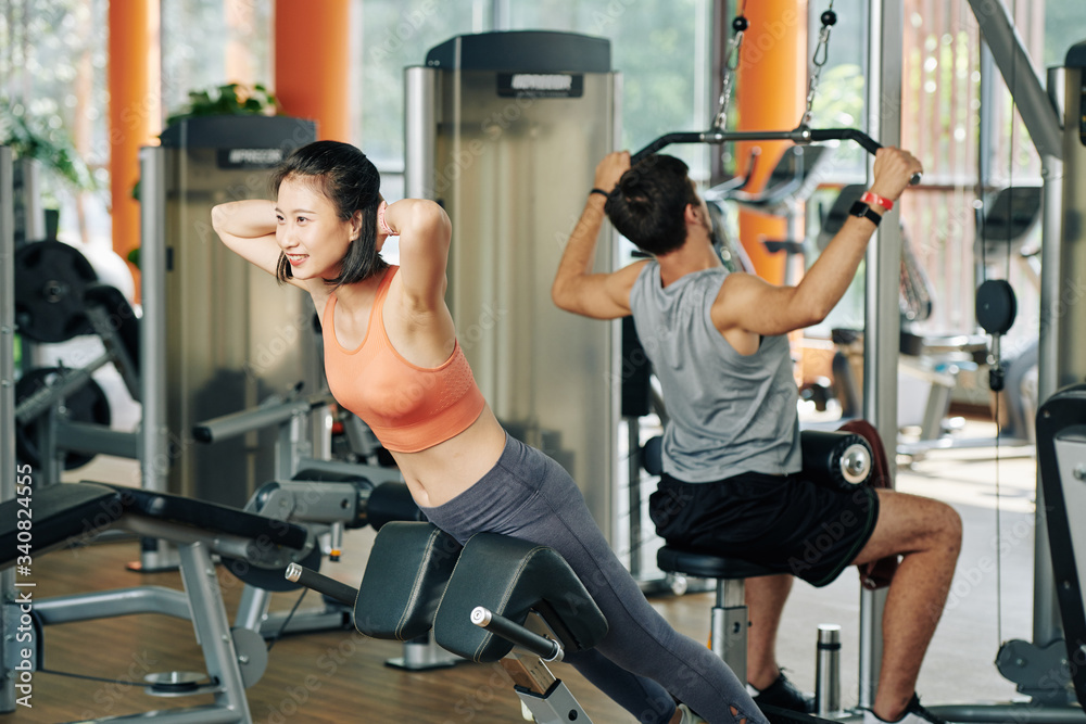 Fototapeta premium Smiling young Vietnamese woman doing hyperextension with hands behind her back