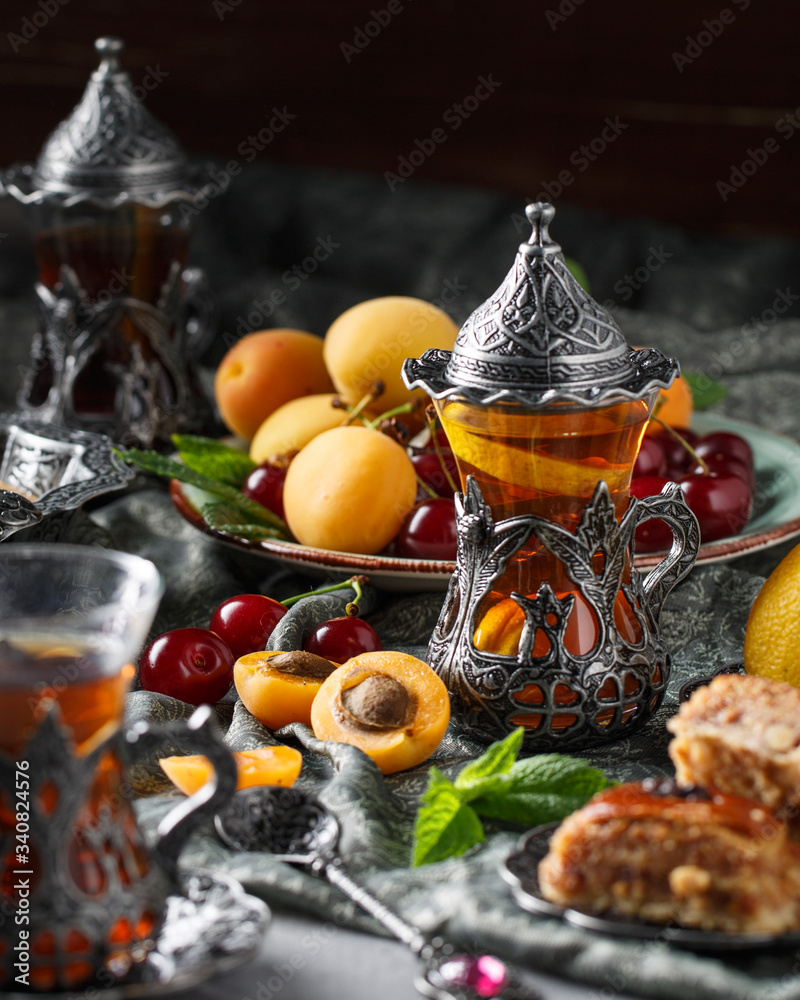 tea armud in Turkish style with lemon. served on a silk tablecloth with baklava and fruit-cherries and apricots