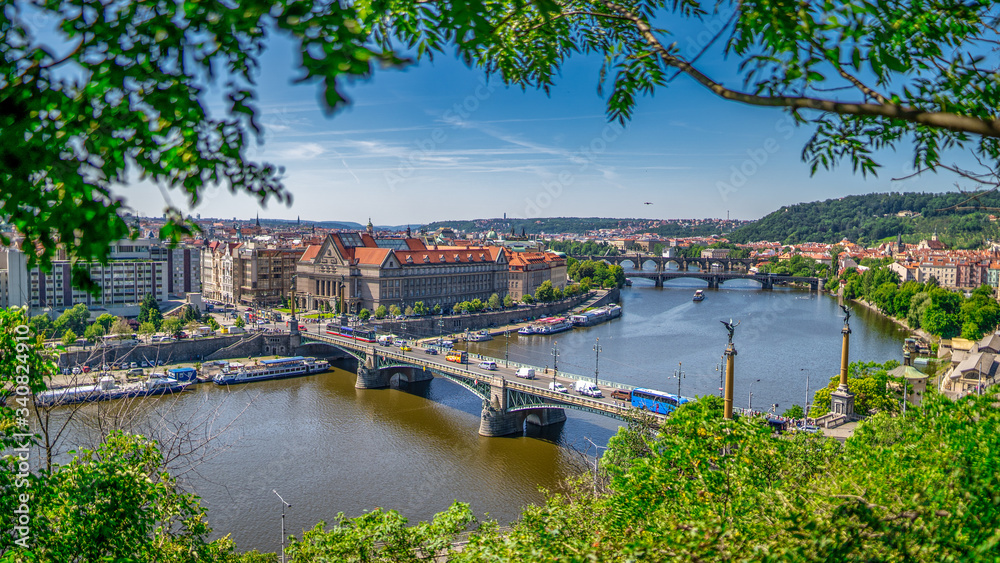 Scenic view of the cityscape, the river Vltava and Charles bridge, Manes and Jirasek bridges across water. Green trees in foreground. 