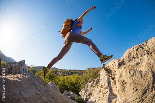 A woman with a backpack jumps over stones.