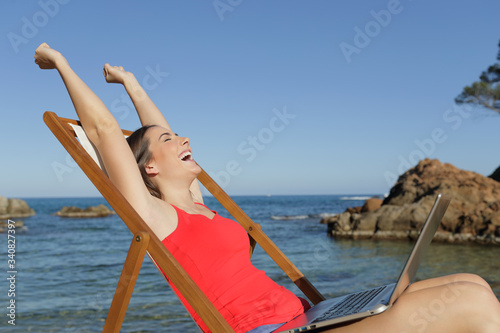 Excited girl celebrating news on laptop on the beach