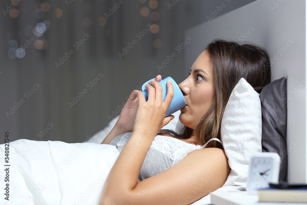 Insomniac woman drinking coffee in bed at night Insomniac woman drinking coffee in bed at night