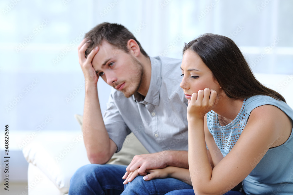 Sad worried couple complaining on a couch at home Sad worried couple complaining on a couch at home
