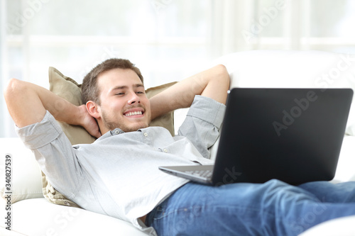 Happy man watching movie on laptop lying on a couch