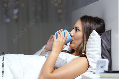 Insomniac woman drinking coffee in bed at night