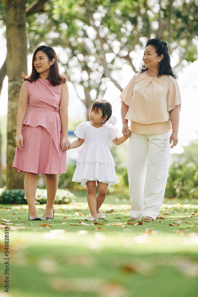 Pretty young smiling grandmother, mother and daughter holding hands when walking in summer park Pretty young smiling grandmother, mother and daughter holding hands when walking in summer park