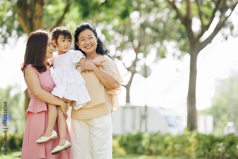 Mother and grandmother carrying adorable little girl when walking in park together Mother and grandmother carrying adorable little girl when walking in park together
