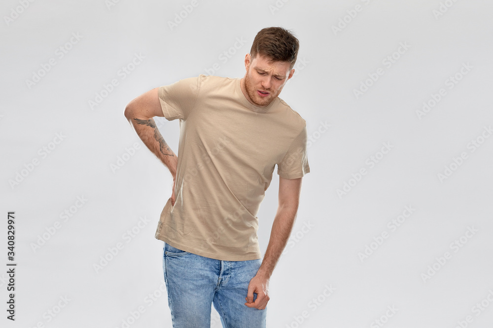 health problem and people concept - unhappy young man suffering from pain in back or reins over grey background health problem and people concept - unhappy young man suffering from pain in back or reins over grey background